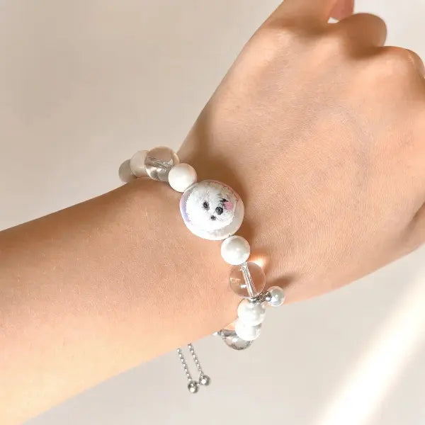 Custom hand-painted pet portrait bracelet featuring a white Bichon Frise dog charm, elegant pearl beads with an adjustable slider chain.