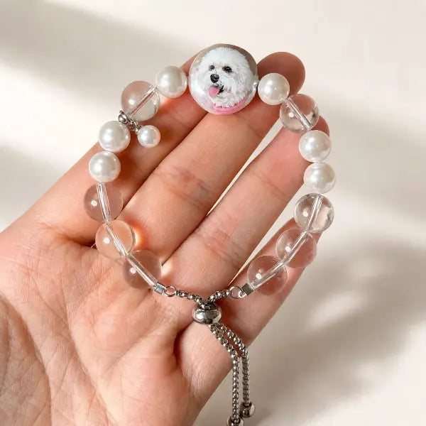 Personalized 100% handmade pet jewelry displaying an adjustable beaded dog portrait bracelet with a mini white puppy replica charm, unique memorial gift.