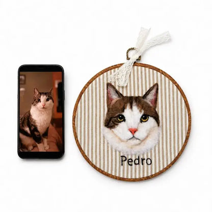 Custom cat photo to felt artwork comparison, showing a smartphone with a tabby and white cat photo next to a handmade 3D needle-felted portrait in a wooden round embroidery hoop.
